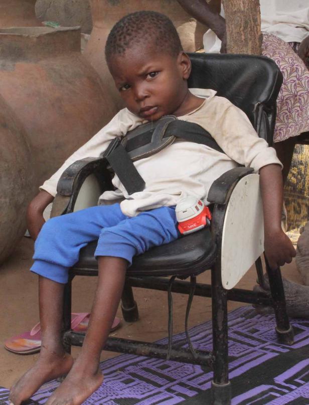 Ein Junge sitzt mit einem Spielzeugauto in einem Stuhl mit Sicherheitsgurt.