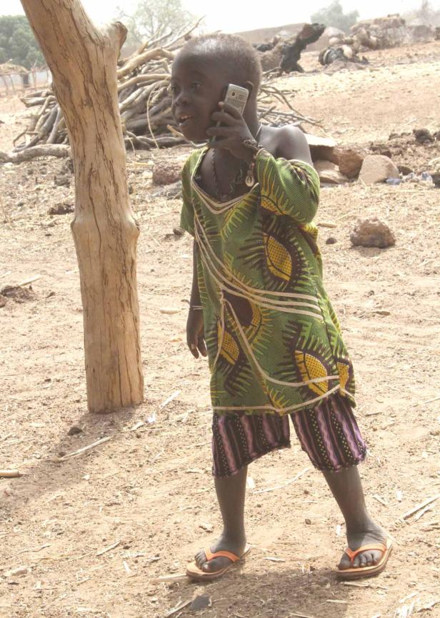 Ein Kind in traditioneller Kleidung telefoniert im Freien.