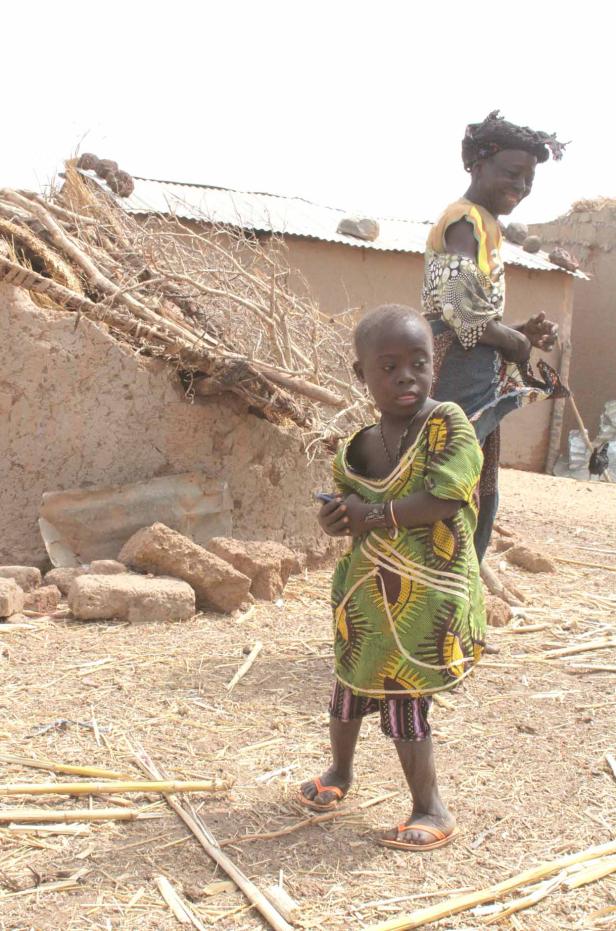 Ein junges Mädchen steht vor einem Haus in einem afrikanischen Dorf.