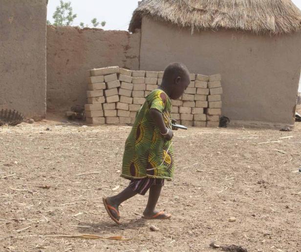 Ein Kind in einem bunten Kleid geht durch ein Dorf.