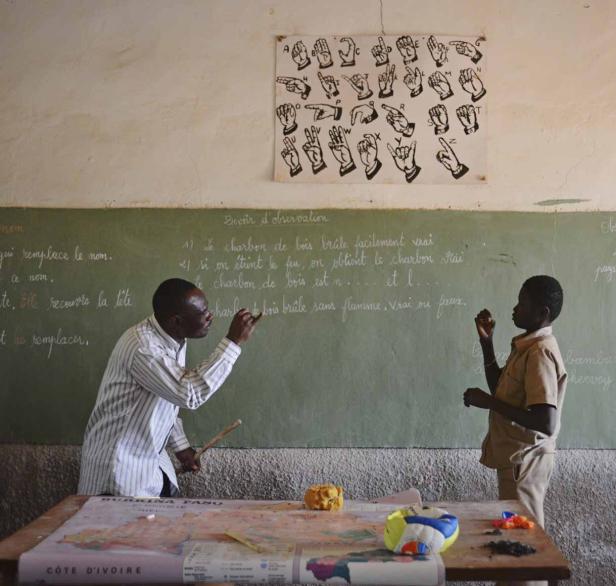 Ein Lehrer erklärt einem Schüler etwas an einer Tafel in einem Klassenzimmer.