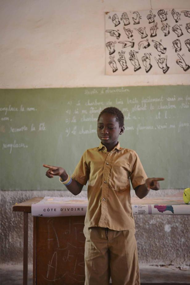 Ein Schüler in Uniform präsentiert vor einer Tafel in einem Klassenzimmer in der Elfenbeinküste.