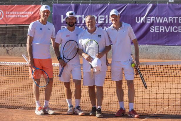 Vier Männer posieren mit Tennisschlägern auf einem Tennisplatz.