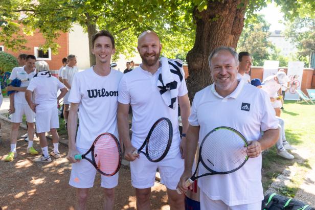 Drei Männer in Sportkleidung posieren mit Tennisschlägern für ein Foto.