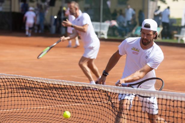 Ein Tennisspieler schlägt den Ball über das Netz auf einem Sandplatz.