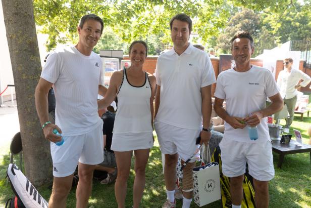 Eine Gruppe von vier Personen in Tenniskleidung posiert im Freien für ein Foto.