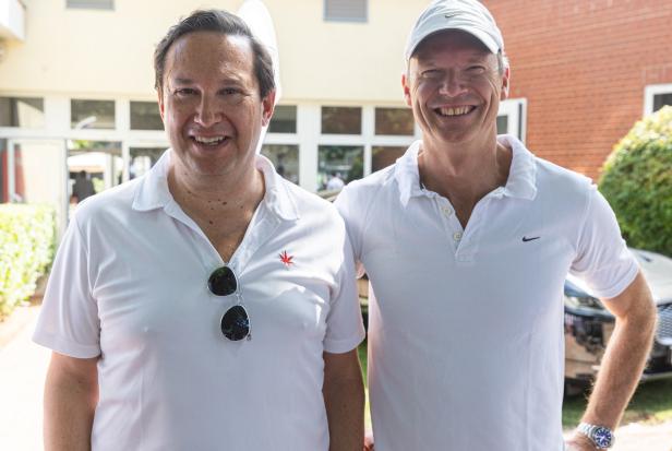 Zwei Männer in weißen Poloshirts lächeln in die Kamera.