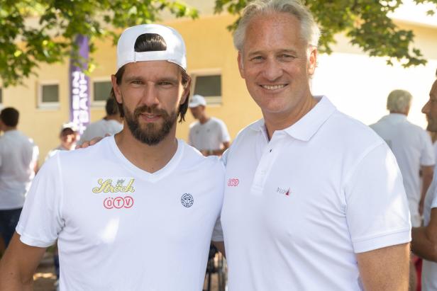 Ein Mann mit Bart und Kappe posiert mit einem Mann im weißen Poloshirt für ein Foto.