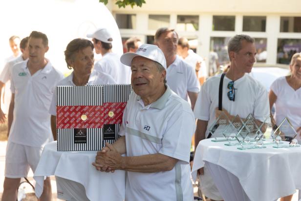 Ein Mann in Sportkleidung steht bei einer Preisverleihung mit Weinpräsenten und Trophäen.