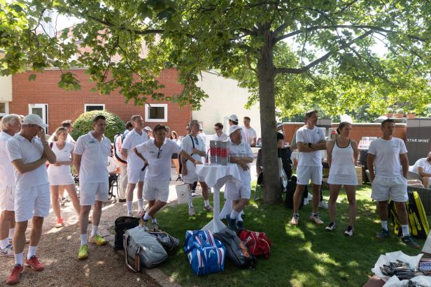 Eine Gruppe von Tennisspielern in weißer Kleidung steht im Freien unter einem Baum.