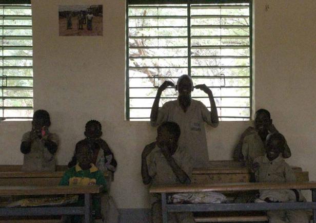 Eine Gruppe Kinder sitzt in einem Klassenzimmer, ein Kind formt mit den Händen Ohren.