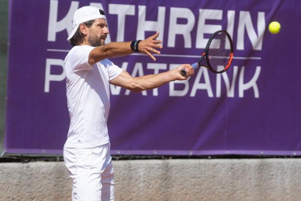 Ein Tennisspieler schlägt einen Ball vor einer lila Werbebande.