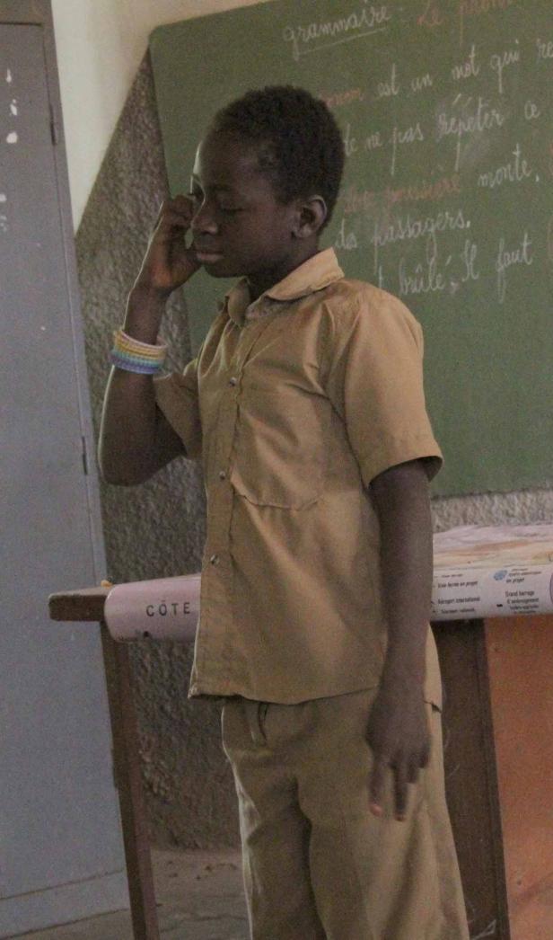 Ein Junge steht vor einer Tafel mit französischer Grammatik.