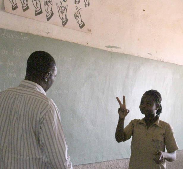 Ein Mädchen zeigt vor einer Tafel das Victory-Zeichen.