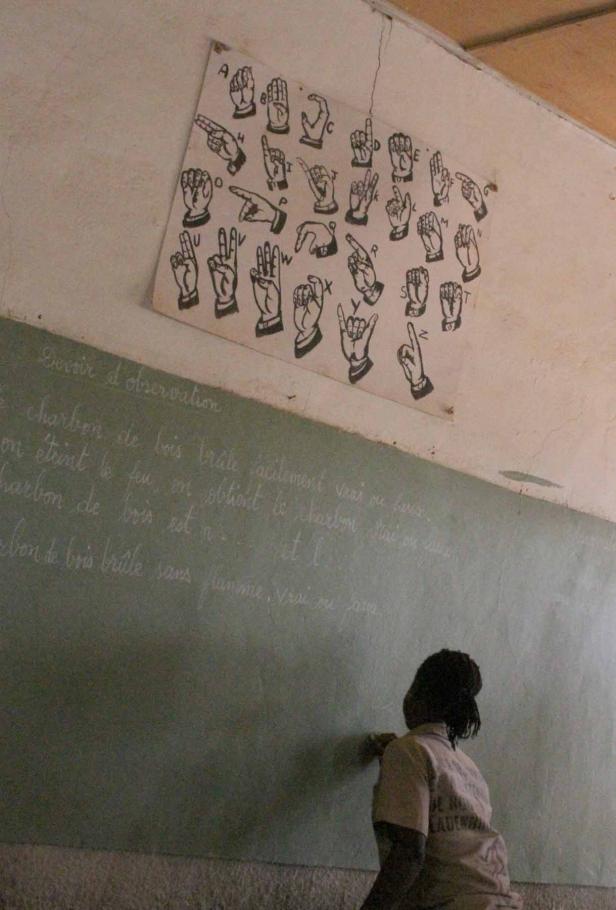 Eine Schülerin schreibt an einer Tafel unter einem Plakat mit Gebärdensprache.