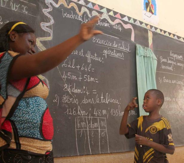 Eine Lehrerin erklärt einem Schüler eine Rechenaufgabe an einer Tafel.