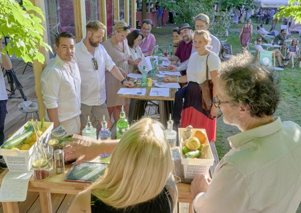 Eine Gruppe von Menschen steht an einem Tisch bei einer Getränkeverkostung im Freien.