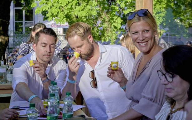 Mehrere Personen sitzen an einem Tisch und probieren Getränke aus kleinen gelben Bechern.