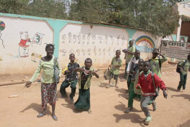 Eine Gruppe Kinder geht an einer mit Bildern und dem Alphabet bemalten Mauer entlang.