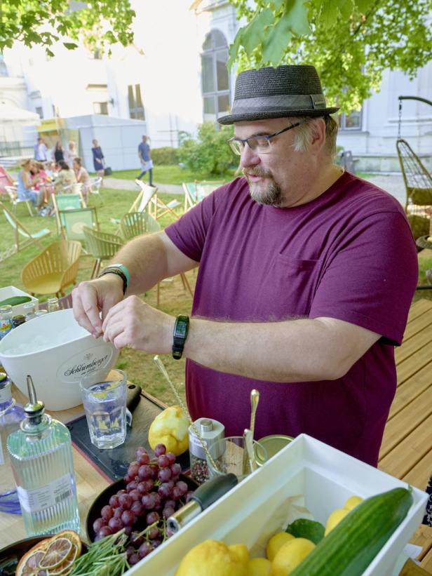 Ein Mann mit Hut bereitet im Freien einen Drink zu.