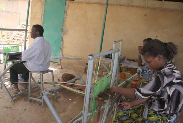 Frauen weben an Webstühlen im Freien.