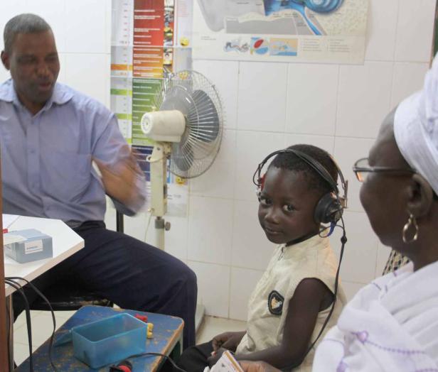 Ein Kind mit Kopfhörern wird von einem Arzt und einer Frau untersucht.