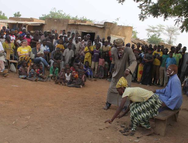 Eine Gruppe von Menschen beobachtet eine traditionelle Zeremonie in einem afrikanischen Dorf.