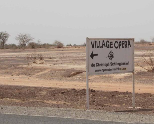 Ein Schild in der afrikanischen Steppe weist auf das „Village Opera“ hin.