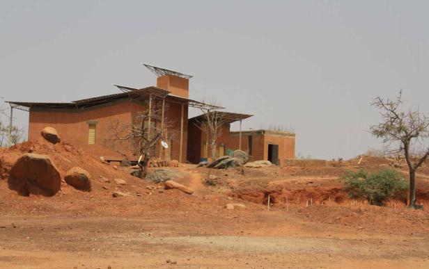 Ein Haus mit Solaranlage in einer trockenen, roten Landschaft.