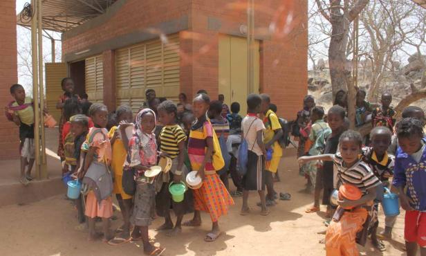 Eine Gruppe afrikanischer Kinder steht vor einem Gebäude mit Tellern und Töpfen in der Hand.