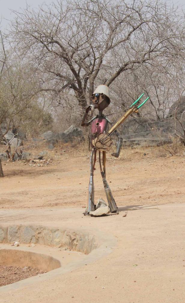 Eine Skulptur aus Metall steht in einer sandigen Landschaft.
