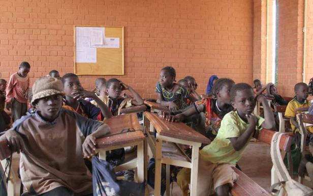 Eine Gruppe afrikanischer Schulkinder sitzt in einem Klassenzimmer an ihren Tischen.