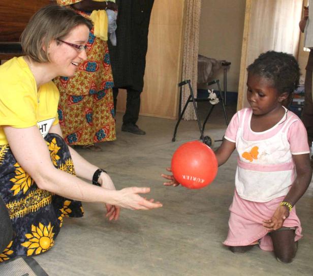 Ein Mädchen kniet und spielt mit einer Frau einen roten Ball zu.