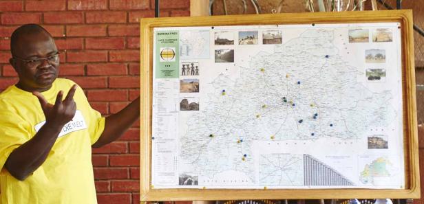 Ein Mann mit einem „Die Welt“-Namensschild gestikuliert vor einer Karte von Burkina Faso.