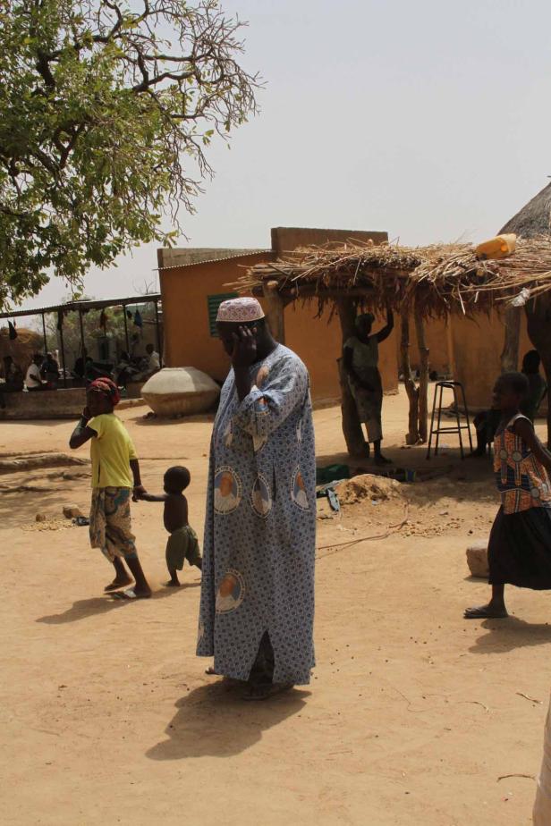 Ein Mann in traditioneller Kleidung telefoniert in einem afrikanischen Dorf.
