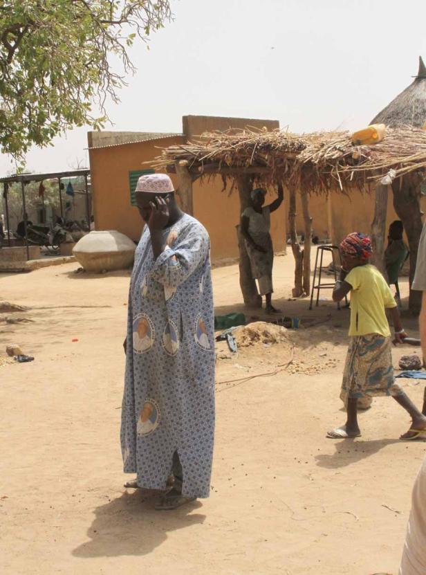 Ein Mann in traditioneller Kleidung telefoniert in einem afrikanischen Dorf.