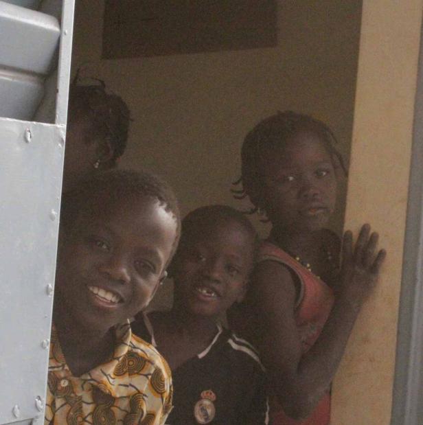 Eine Gruppe afrikanischer Kinder schaut aus einem Gebäude.