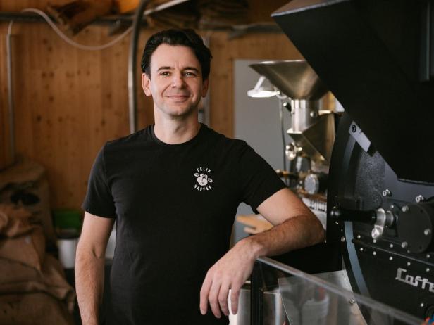 Ein Mann mit einem T-Shirt der Marke „Felix Kaffee“ steht neben einer Kaffeeröstmaschine.