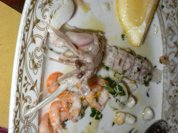 Auf einem Teller liegen Garnelen, eine Seespinne und eine Zitronenspalte.