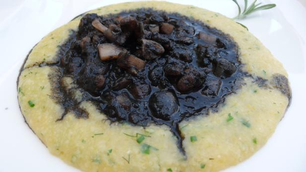 Polenta mit Tintenfischtinte und Tintenfischstücken auf einem Teller.