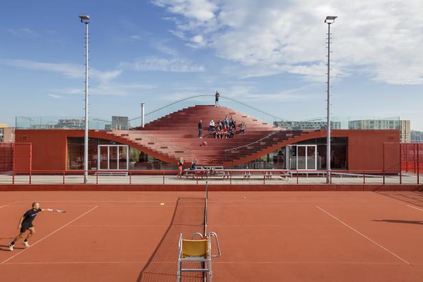 Ein Tennisplatz mit Zuschauern auf einer wellenförmigen Treppe im Hintergrund.
