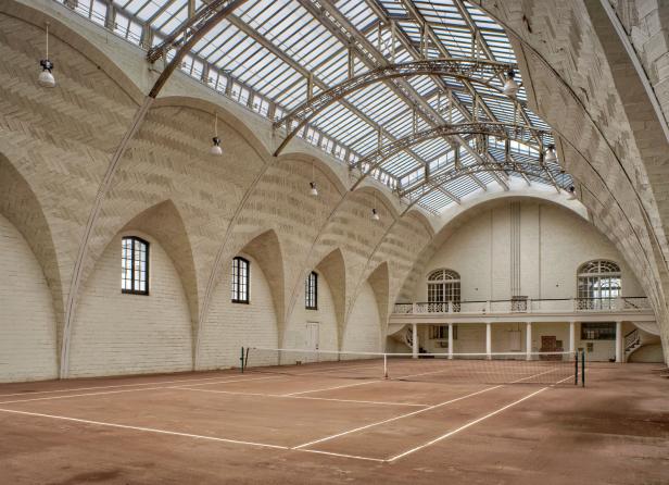 Ein leerer Tennisplatz in einer Halle mit einem Glasdach.