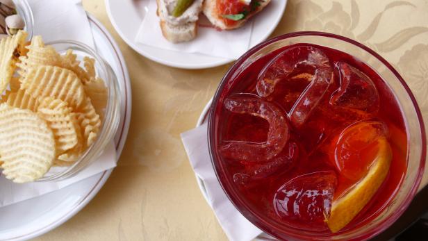 Ein Aperol Spritz mit Eis und einer Orangenscheibe, dazu Chips und Bruschetta.