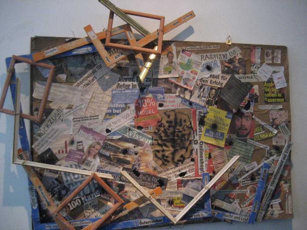 Eine Collage aus Zeitungsausschnitten, Holzrahmen und anderen Materialien auf einer braunen Platte.