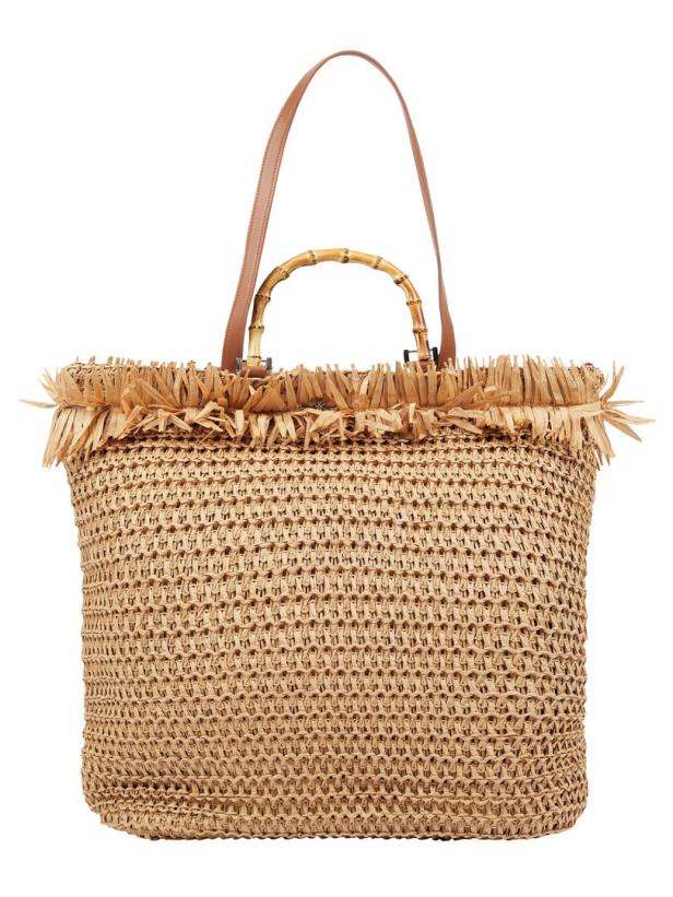 Eine große Strandtasche aus Bast mit Bambusgriffen und braunen Lederriemen.