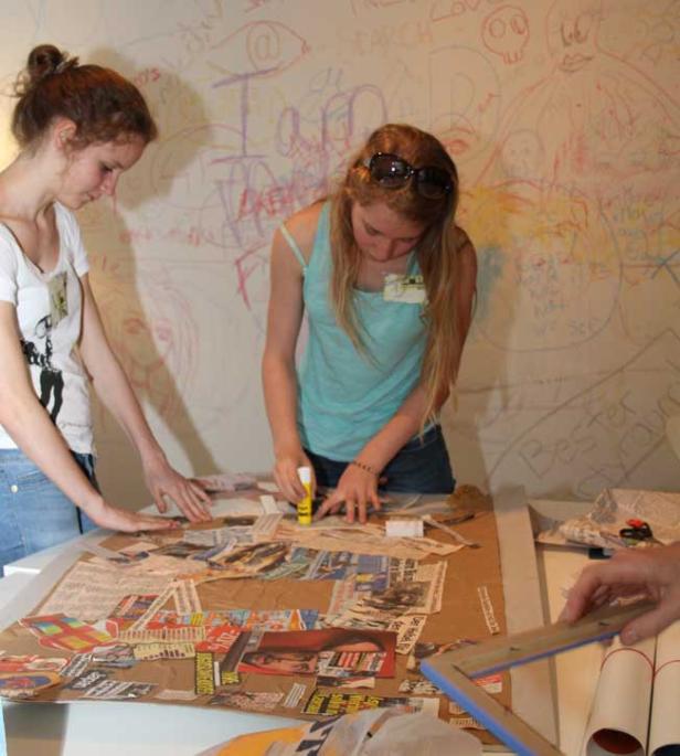 Zwei junge Frauen erstellen eine Collage aus Zeitungsausschnitten auf einem Tisch.