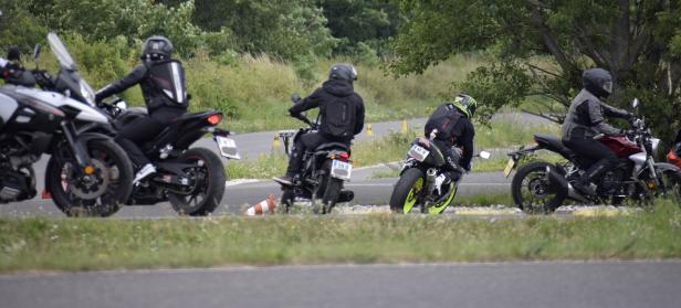 Mehrere Motorradfahrer fahren auf einer asphaltierten Straße an gelben Hütchen vorbei.