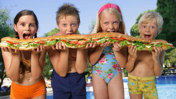 Vier Kinder halten gemeinsam ein sehr langes Sandwich in der Hand.