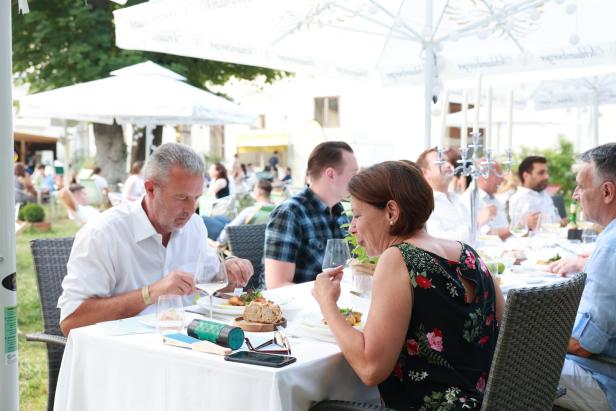 Menschen sitzen an einem Tisch im Freien und essen zu Mittag.