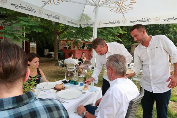 Zwei Kellner servieren Speisen an einem Tisch im Freien.